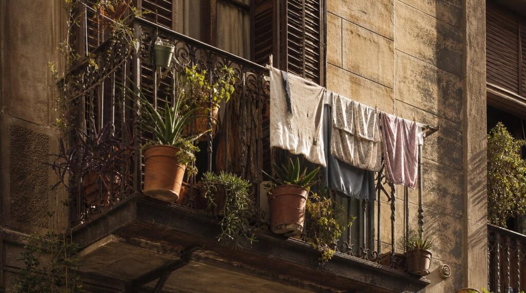 Close, textural shot of a small balcony in a Barcelona apartment building, potted plants and hanging laundry in warm afternoon