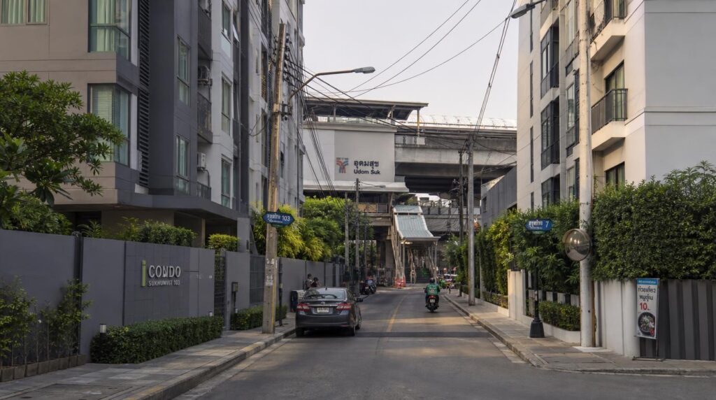 A residential Bangkok side street with modern low-cost condo buildings, a BTS station