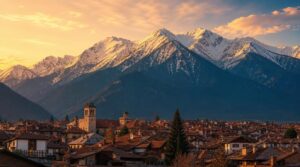 Wide landscape shot of Bansko's rooftops nestled at the base of the snow-capped Pirin Mountains, golden late-afternoon light