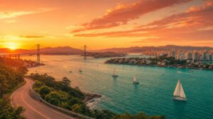 Wide landscape shot of Florianopolis island at golden hour, seen from an elevated coastal road, the Hercílio Luz suspension
